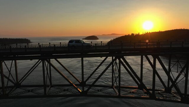 Drone shot of an SUV driving through the sunset's glow on Deception Pass.