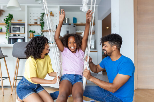 Mom And Dad Swinging And Having Fun With Their Daughter At Home.