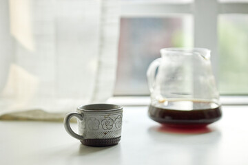 coffee cup and coffee pot before window