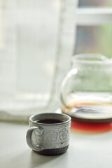 coffee cup and coffee pot before window