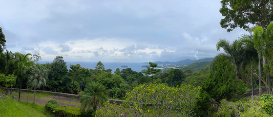 Wide panorama. Tropical island. Green forest and sea. Top view. Sky with clouds and lightening. Thunderstorm is coming. Horizontal frame. Andaman. Phuket Thailand. Karon Viewpoint. Beautiful landscape