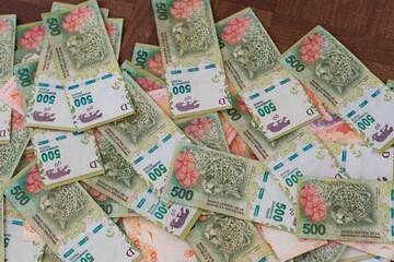 Billetes de 500 pesos argentinos desparramados sobre fondo de madera marron