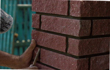 The bricklayer aligns the seams using a wooden stick.