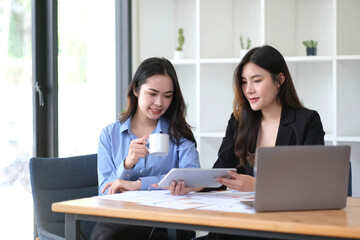 Two young Asian businesswoman discuss investment project working and planning strategy. Business people talking together with laptop computer at office.