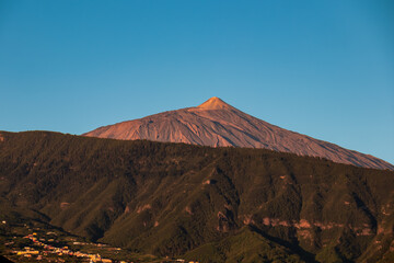 Fototapeta na wymiar Panoramic view on the peak of volcano Pico del Teide during sunrise seen from the port of Puerto de la Cruz, Tenerife, Canary Islands, Spain, Europe. The summit turns vibrant red during golden hour