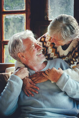Happy senior couple hug and enjoy time together at home sitting on che chair and smiling each...