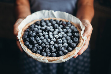 Close up of woman hands holding a blueberries cake pie handmade at home. Traditional bakery artisan concept. Tasty and seasonal antioxidant berries tasty cake. Dark background homemade food concept