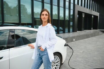 Woman near electric car. Vehicle charged at the charging station.