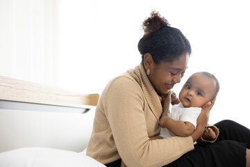 African young mother carrying and kissing with her adorable baby on bed