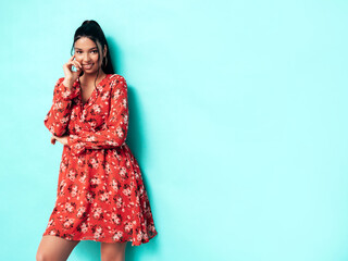 Young beautiful smiling female in trendy summer red dress clothes. Sexy carefree woman posing near blue wall in studio. Positive model having fun and going crazy. Cheerful and happy