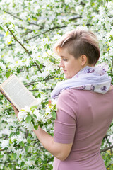 A beautiful woman in pink clothes walks through a spring park. Reading a book