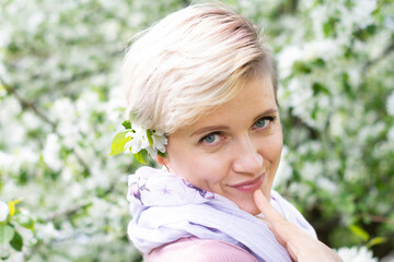 young woman with pink hair poses by a blooming apple tree.