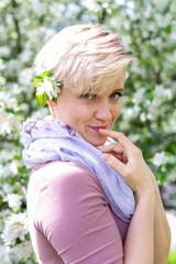 young woman with pink hair poses by a blooming apple tree.