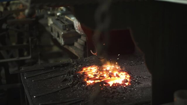 Fire is burning at the workplace of a blacksmith, moving chains with hand to produce air flow.