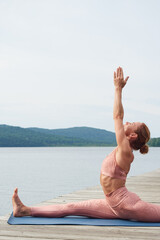 Sportswoman in pink sportswear practicing yoga on the seashore