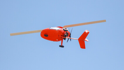 Red helicopter in flight on a blue sky.