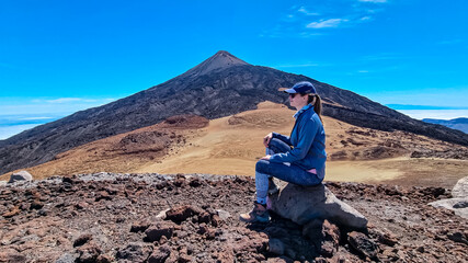 Hiking woman sitting on rock on summit of Pico Viejo looking at scenic view on the peak of volcano Pico del Teide, Tenerife, Canary Islands, Spain, Europe. Volcanic barren solidified lava terrain. Awe