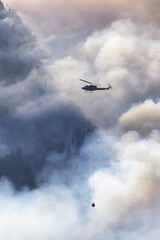 Fototapeta na wymiar Wildfire Service Helicopter flying over BC Forest Fire and Smoke on the mountain near Hope during a hot sunny summer day. British Columbia, Canada. Natural Disaster