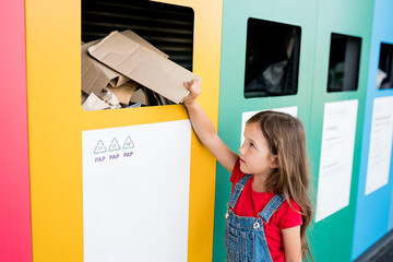 Girl recycling cardboard in paper bank. Children putting papers in recycling bin. Sustainble...