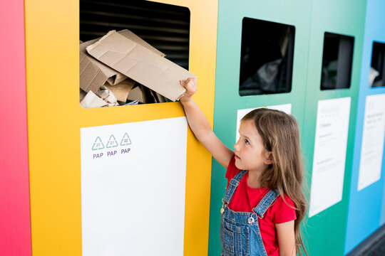 Girl recycling cardboard in paper bank. Children putting papers in recycling bin. Sustainble lifestyle concept. - Powered by Adobe