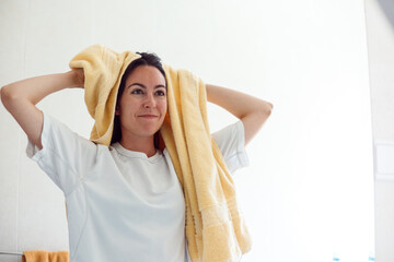 Real young woman drying wet hair with towel, being pleased after taking bath, poses against white background, has cheerful expression