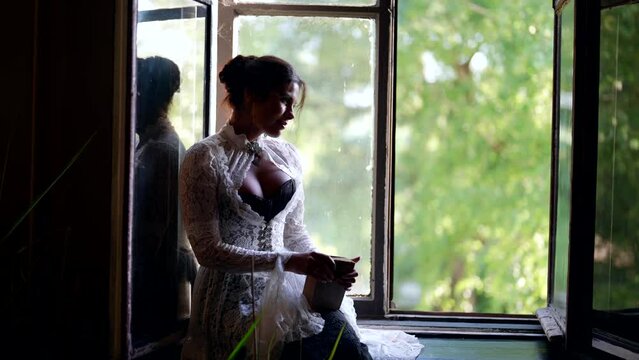 romantic young lady from past century is sitting near open window of noble estate in summer