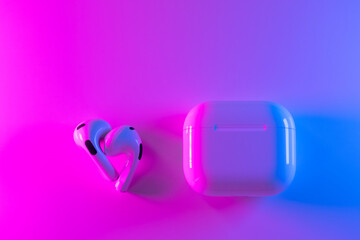 White modern headphones wireless earphones with case, copy space neon pink and blue background