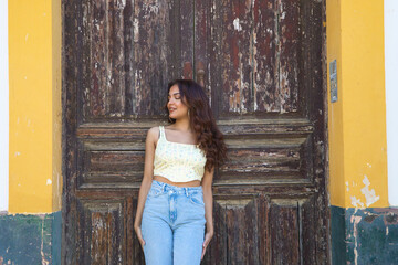 Fototapeta premium Young beautiful woman dressed in casual clothes leaning on an old door of an old house in seville. The woman is making different expressions and postures and is on holiday enjoying her holiday.