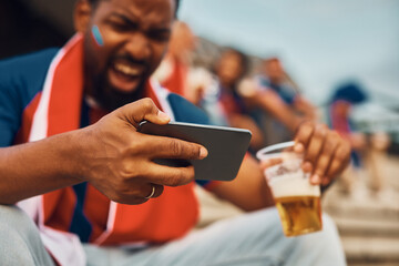 Close up of black man cheering while watching football match on mobile phone.