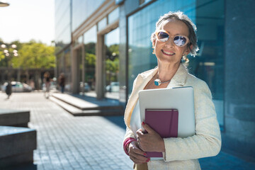 Middle-aged confident, focused and powerful business woman looking at camera. Beautiful mature lady smiling with sunglasses, books and tablet.