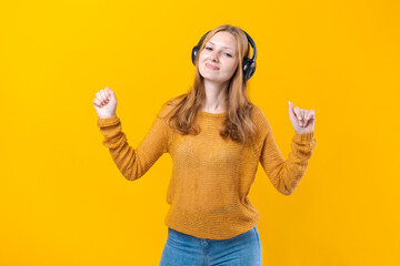 Woman dancing to music while listening to MP3 player with wired headphones. Energy move of caucasian dancer isolated on yellow background. Happy girl rejoices at free time in the studio