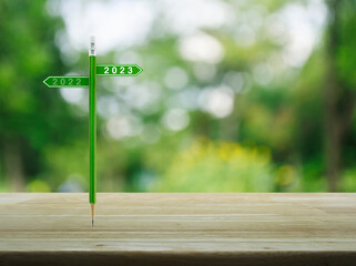 2023 and 2022 direction sign plate with green pencil on wooden table over blur green tree in park,...