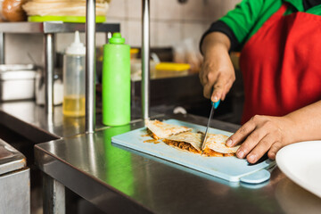 Worker slicing a piece of mexican taco in a kitchen of a restaurant