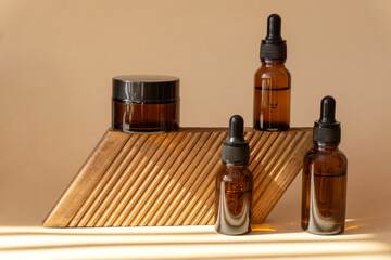 Mockup of amber glass bottles with serum, jars of hand cream, faces on geometric reflexed stand in rays of sunlight. Concept of 3d podium for the demonstration of cosmetics