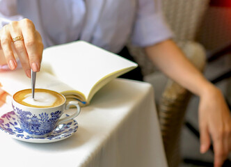 A cup of capicino with a blue pattern on a table in a cafe. Female figure sitting in a cafe.