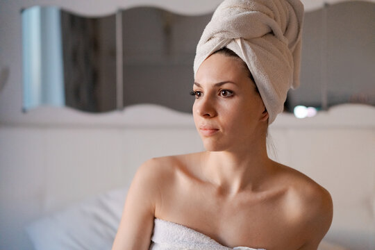 Portrait smiling young European brunette woman enjoying her spa in evening before going to bed in bed. Happy girl in a towel in the bedroom. Skin care beauty