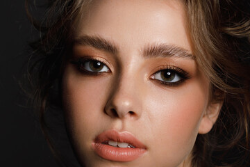 Obraz premium Young beauty with well-groomed eyebrows and professional make-up on a black background, close-up