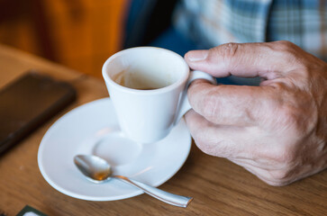 Hands of old man holding cup of coffee on the wood table