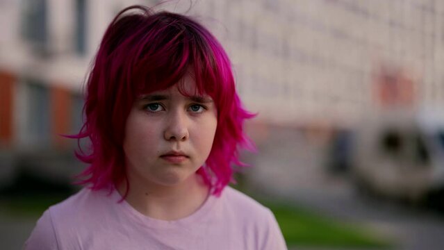 shy and incredulous teen girl with colored pink hair is looking at camera, outdoors portrait in big city