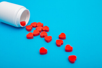 Red heart shaped pills with plastic bottle on blue background.Concept love addiction, love drugs, Valentine's Day and depression