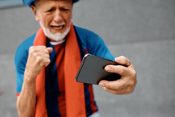 Close up of senior man watching soccer match on smart phone.