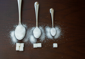 Sugar in spoons of different sizes, sugar cubes in front of them. The amount of sugar, the concept of reducing sugar use.