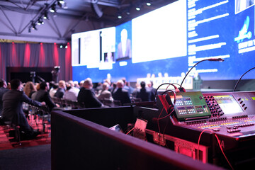 Technician handling the lights at a conference with an anonymized blurry audience and stage in the background