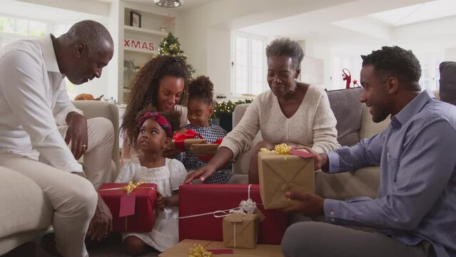 Multi-generation family celebrating Christmas at home sitting in lounge opening presents together - shot in slow motion