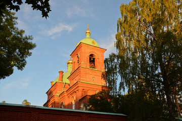 Fototapeta premium Beautiful Resurrection Skete of the Valaam Monastery. Horizontal photo of a red brick temple at sunset