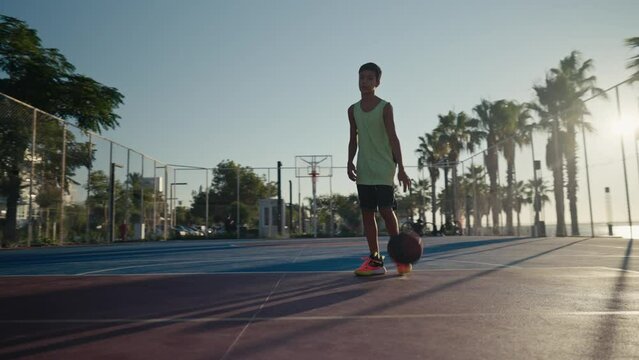 12 year old boy bouncing basketball ball training on ground floor of the court. Basketball player. Workout. Sport activities. High quality 4k footage