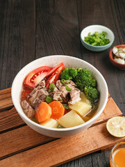 Soup, Sop Daging with vegetables is Indonesian traditional food, served in bowl, on the wooden table. Close up and selective image focus.
