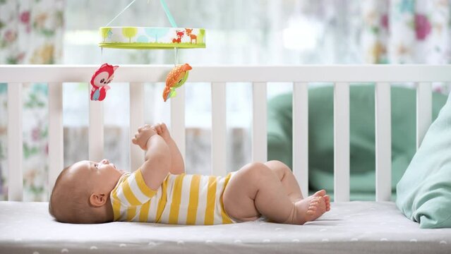 The three month baby in the crib looking at the mobile carousel and smiling. Happy child. Newborn is in the crib. Mobile for children.