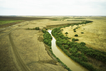 Naklejka premium a winding muddy river with overgrown green banks in a sun-scorched steppe rural landscape