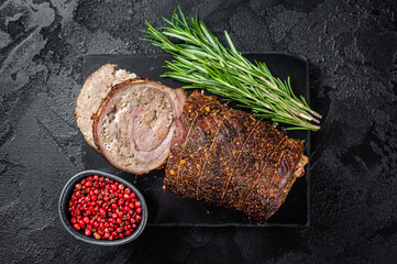 Baked pork roulade  Porchetta, rolled pork meat on a marble board with herbs. Black background. Top...